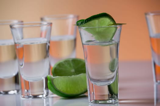 Tequila shot with a slice of lime on the glass on orange background. Selective Focus