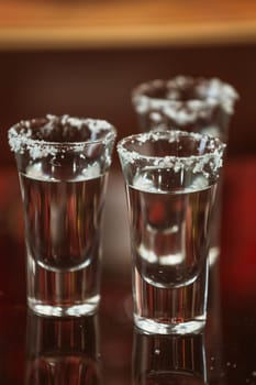 two shots of tequila with lime and salt on a wooden table bar on the background of bright lights of the bar