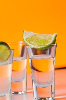 Tequila shot with a slice of lime on the glass on orange background. Selective Focus