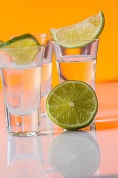 Tequila shot with a slice of lime on the glass on orange background. Selective Focus