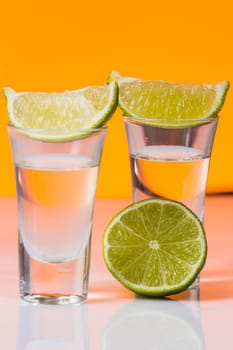 Tequila shot with a slice of lime on the glass on orange background. Selective Focus