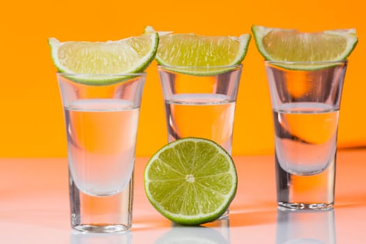 Tequila shot with a slice of lime on the glass on orange background. Selective Focus