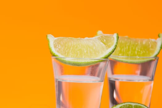 Tequila shot with a slice of lime on the glass on orange background. Selective Focus