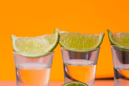 Tequila shot with a slice of lime on the glass on orange background. Selective Focus