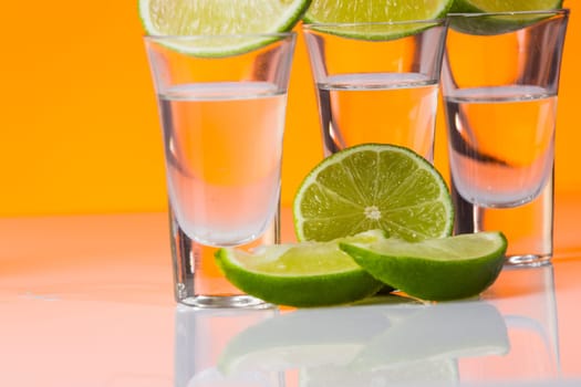 Tequila shot with a slice of lime on the glass on orange background. Selective Focus