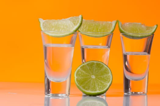 Tequila shot with a slice of lime on the glass on orange background. Selective Focus