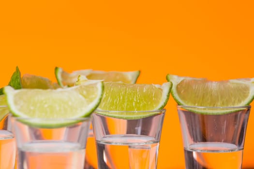 Tequila shot with a slice of lime on the glass on orange background. Selective Focus