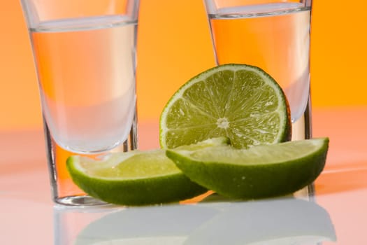 Tequila shot with a slice of lime on the glass on orange background. Selective Focus