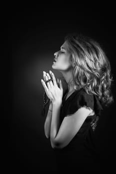 Dramatic black and white portrait of a woman praying or thinking emerging from a black background