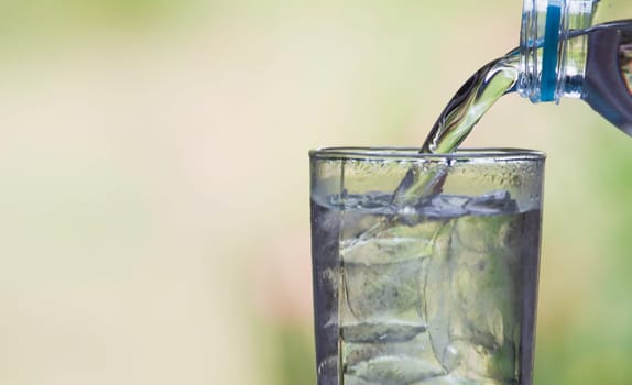 Female hand pouring water from bottle to glass on blur background