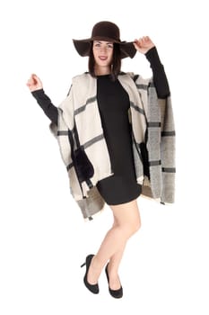 A beautiful woman standing is a black dress and high heels with a big .poncho over her shoulder and black hat, isolated for white background.