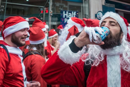 London, UK - December 2018 : Man dressed in santa outfit drinking alcoholic beer from a can while taking part in a themed SantaCon event