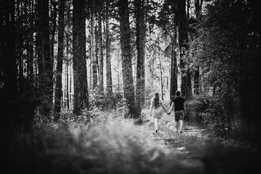Black white photography romantic young couple go and holding hands on background summer forest
