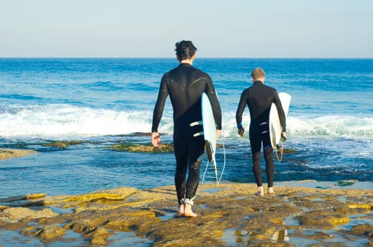 Professional surfers carrying their surfboards while going to the sea, professional surfers in black diving suits ready to surf walk to the ocean.
