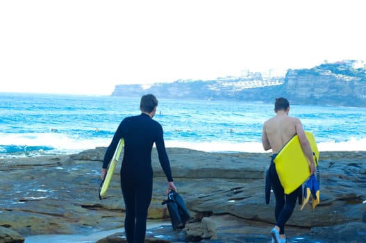 Professional surfers carrying their surfboards while going to the sea, professional surfers in black diving suits ready to surf walk to the ocean.