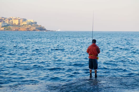 A fisherman in a red rain jacket fishing along the Bondi beach, Sydney, Australia.