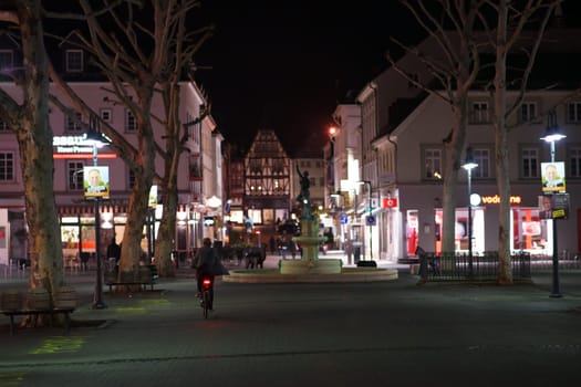 Limburg, Germany - November 03, 2018: A cyclist driving through the city center of Limburg at night with illuminated shops on November 03, 2018 in Limburg..