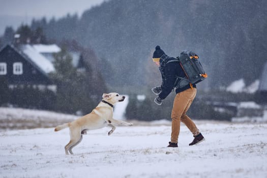 Friendship between pet owner and his dog. Young man playing with labrador retriever in winter landscape. Jizera mountains, Czech Republic