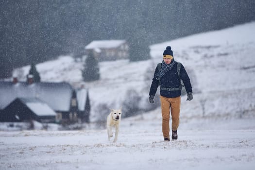 Friendship between pet owner and his dog. Young man walking with labrador retriever in winter landscape. Jizera mountains, Czech Republic
