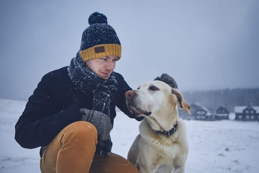 Friendship between pet owner and his dog. Young man stroking labrador retriver in winter landscape.