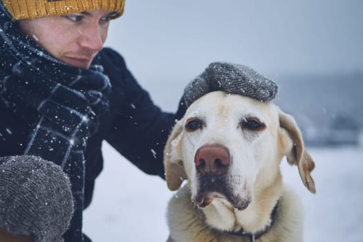Friendship between pet owner and his old dog. Young man stroking labrador retriver in winter landscape.