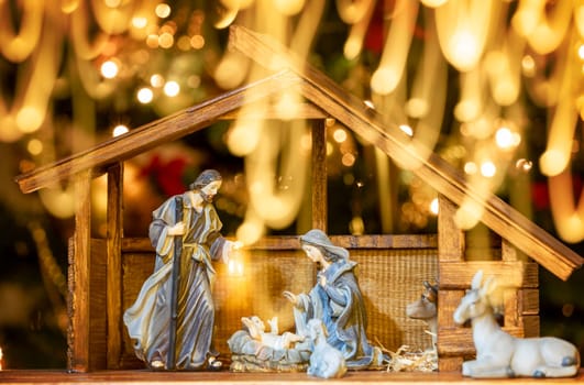 Christmas Manger scene with figurines including Jesus, Mary, Joseph, sheep and wise men. Focus on mother! Lights train in front of photo camera.