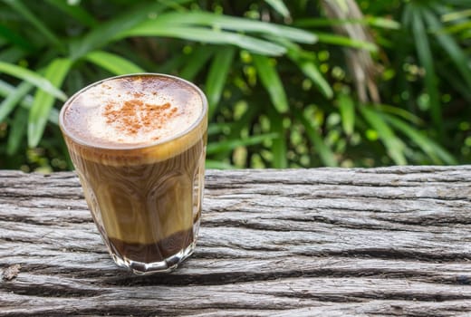Latte Coffee in Glass on Wood Table with Natural Green Tree Background Left. Latte coffee in coffee shop or cafe. with nature green tree .relax emotion background
