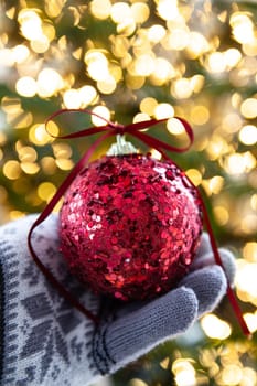 Hand holding a festive Christmas bauble in front of bokeh lights