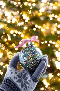 Hand holding a festive Christmas bauble in front of bokeh lights