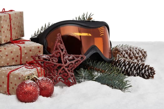 Winter holidays still life with gift boxes, fir tree branch, ski glasses and Christmas decorations lying on snow on a white background. New Year and Christmas. Winter vacation.