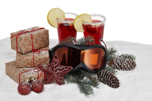 Winter holidays still life with gift boxes, fir tree branch, ski glasses, mulled wine and Christmas decorations lying on snow on a white background. New Year and Christmas. Winter vacation.