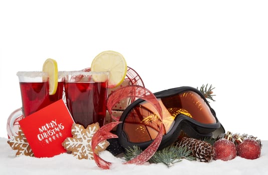 Winter holidays still life with fir tree branch, ski glasses, fruit tea, gingerbread cookies and Christmas decorations lying on snow with copy space. Christmas Greeting card. Winter vacation.
