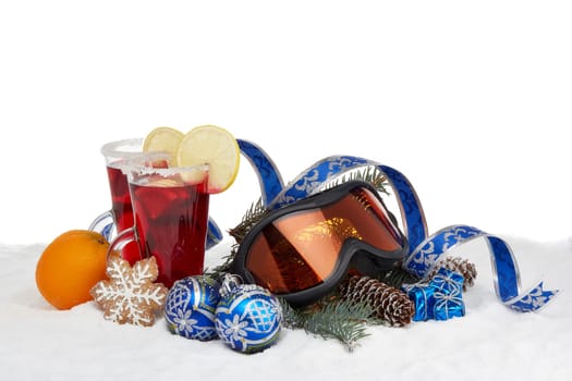 Winter holidays still life with fir tree branch, ski glasses, fruit tea and Christmas decorations lying on snow on a white background with copy space. New Year and Christmas. Winter vacation.