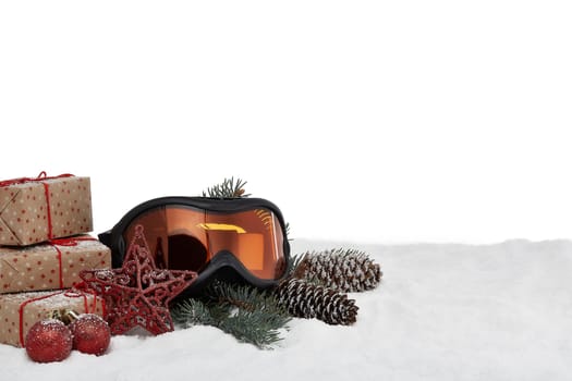 Winter holidays still life with gift boxes, fir tree branch, ski glasses and Christmas decorations lying on snow on a white background with copy space. New Year and Christmas. Winter vacation.