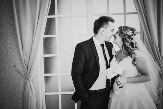 Black white photography bride and groom posing in a hotel room on background windows