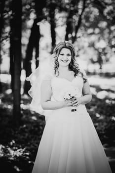 Black white photography stylish beautiful happy bride holding bouquet of flowers on a background of trees in the summer park close-up