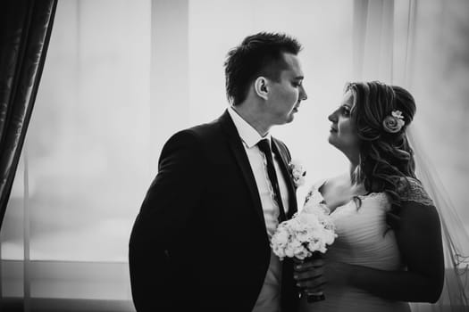 Black white photography bride and groom posing in a hotel room on background windows