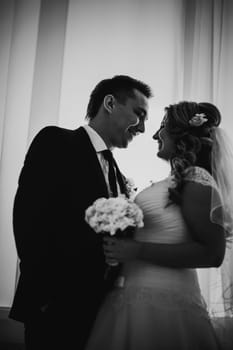 Black white photography bride and groom posing in a hotel room on background windows