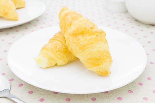Croissant or bread or bakery on white dish on pink point placemat with spoon and tea cup and soup cup