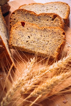 Close slice of fresh bread with poppy seeds and wheat ears on wooden background