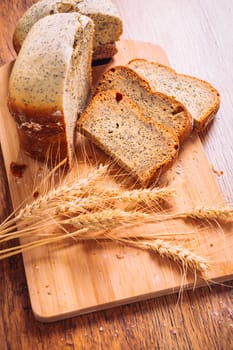 Close slice of fresh bread with poppy seeds and wheat ears on wooden background