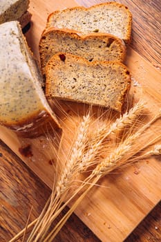 Close slice of fresh bread with poppy seeds and wheat ears on wooden background