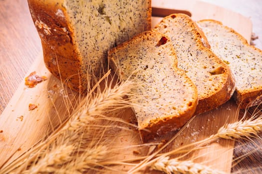 Close slice of fresh bread with poppy seeds and wheat ears on wooden background