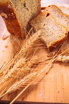 Close slice of fresh bread with poppy seeds and wheat ears on wooden background