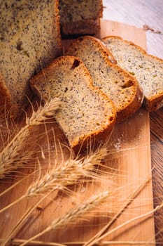 Close slice of fresh bread with poppy seeds and wheat ears on wooden background