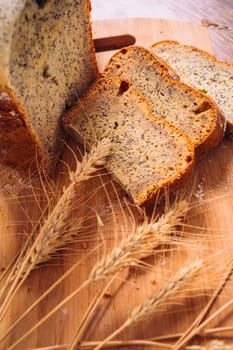 Close slice of fresh bread with poppy seeds and wheat ears on wooden background