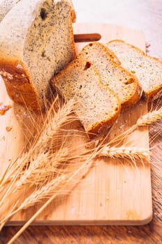 Close slice of fresh bread with poppy seeds and wheat ears on wooden background