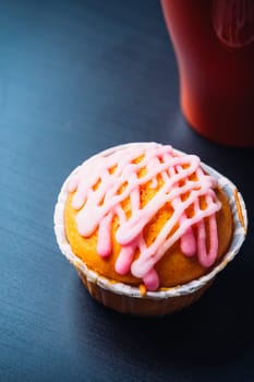 cupcake with pink frosting and red cup on a wooden background
