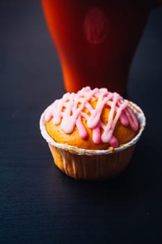 cupcake with pink frosting and red cup on a wooden background