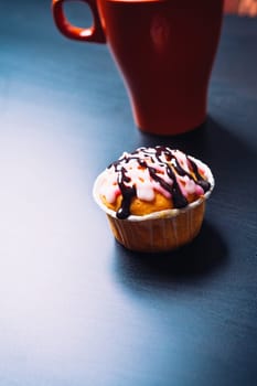 cupcake with pink frosting and red cup on a wooden background